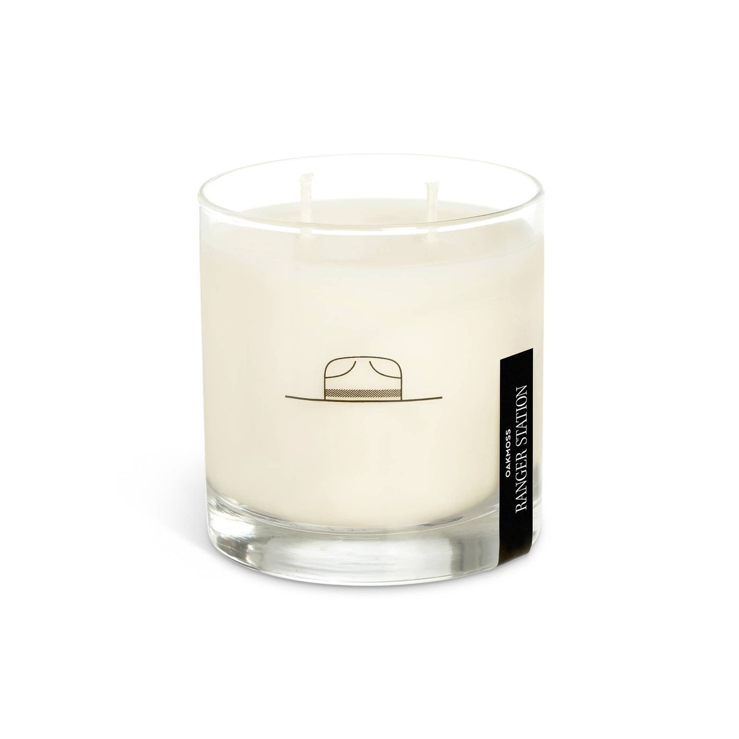 A white candle in a clear glass container with a black lid, featuring a label with a hat illustration and the brand name 'Ranger Station'.