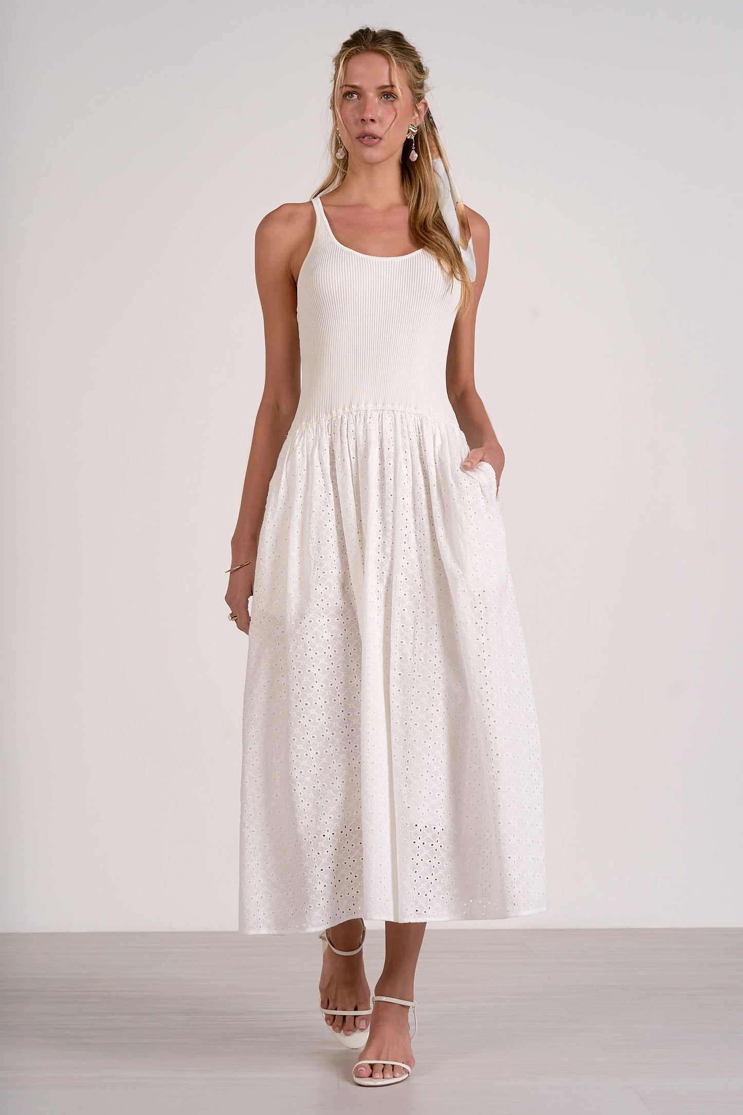 Woman wearing a white sleeveless dress with lace details on a plain background