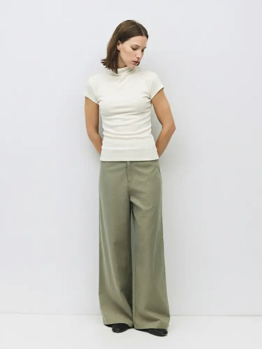 Woman wearing a white top and green pants against a plain background