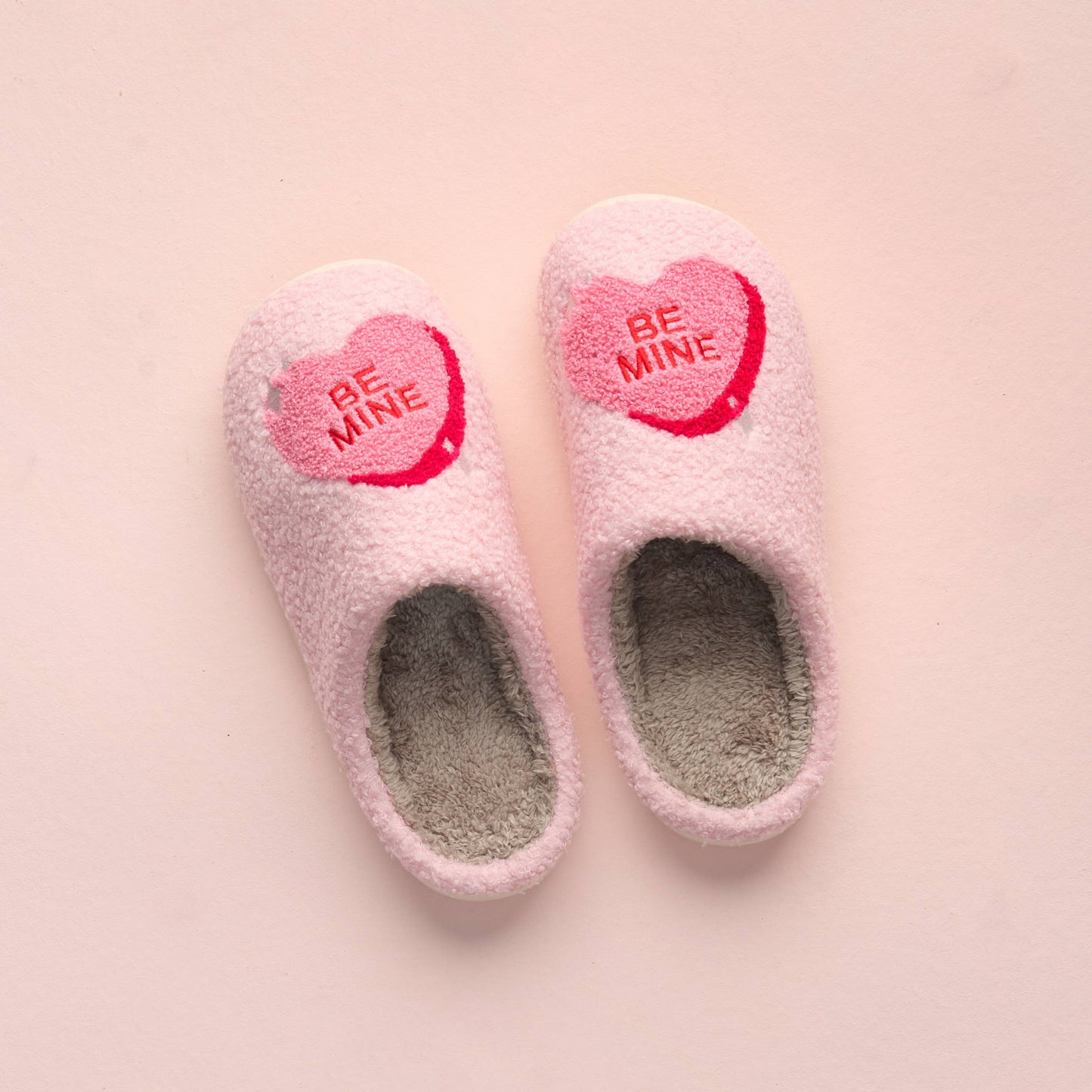 Pink slippers with 'Be Mine' heart labels on a pink background