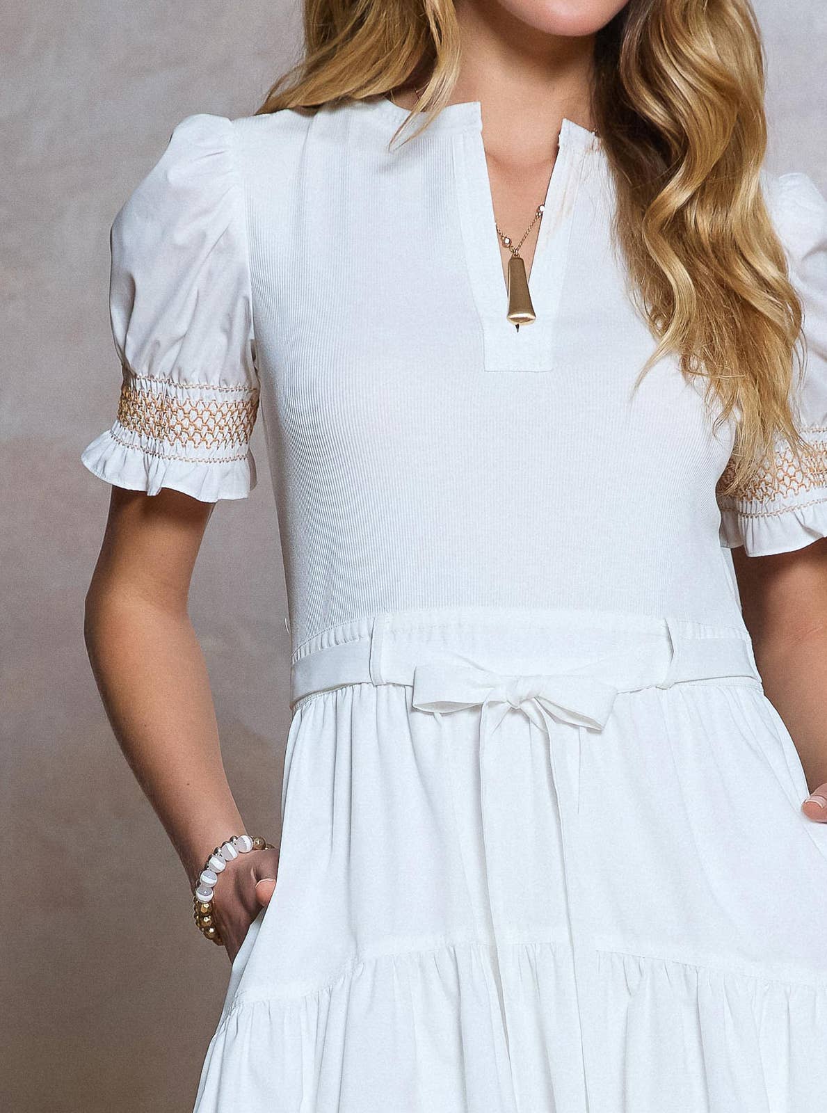 White dress with lace details on sleeves and waistband against a neutral background