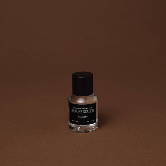 Perfume bottle with black cap and label on a brown background. Label says: Ranger Station Oakmoss