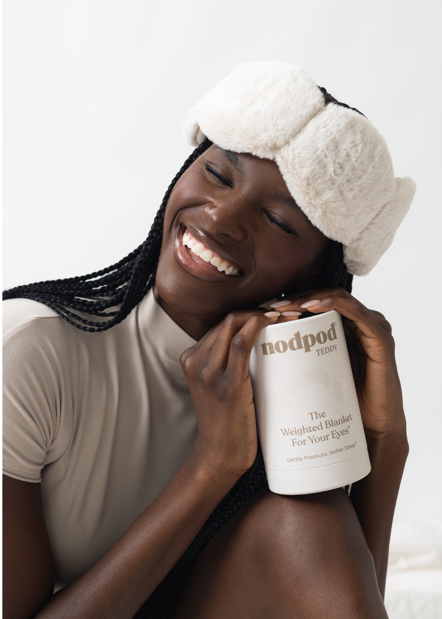 Woman wearing a white eye mask and holding a Nodpod product on a plain background