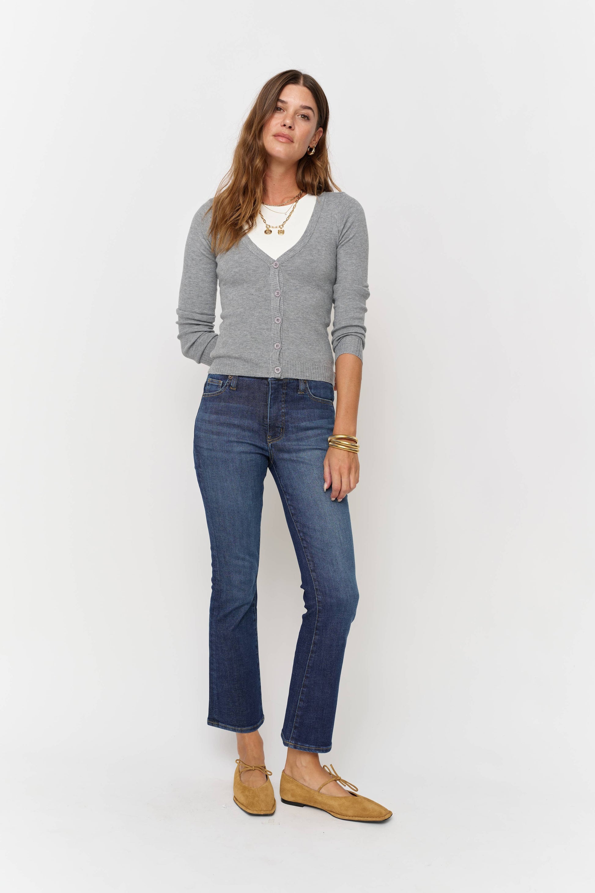 Woman wearing a gray sweater, white shirt, blue jeans, and brown shoes on a white background