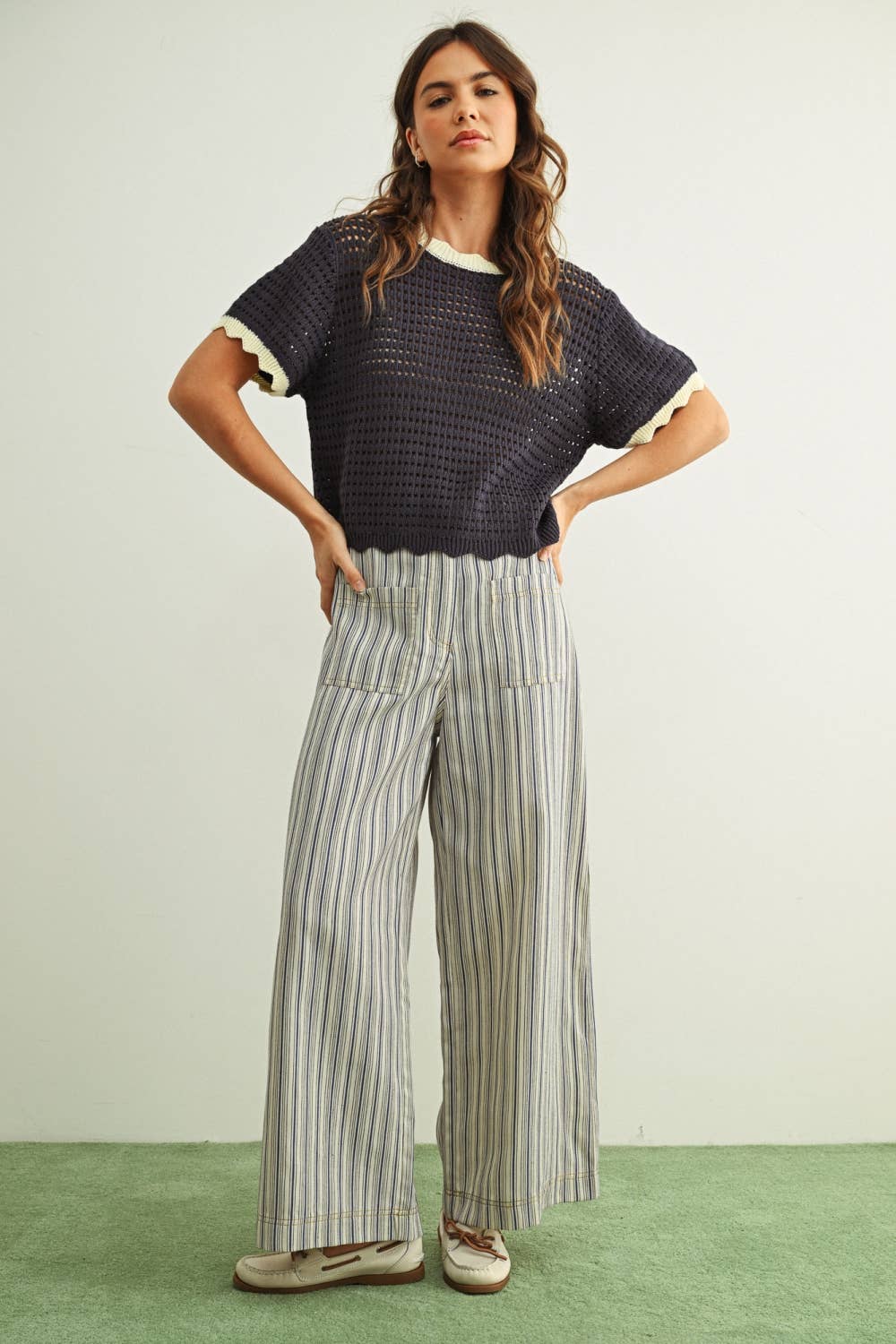 Woman wearing a dark blue top and striped pants on a light green background