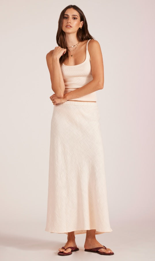 Woman wearing a light pink sleeveless top and white skirt on a plain background