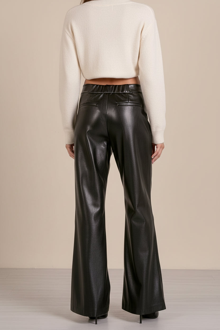 Person wearing black leather pants and a white sweater against a beige background