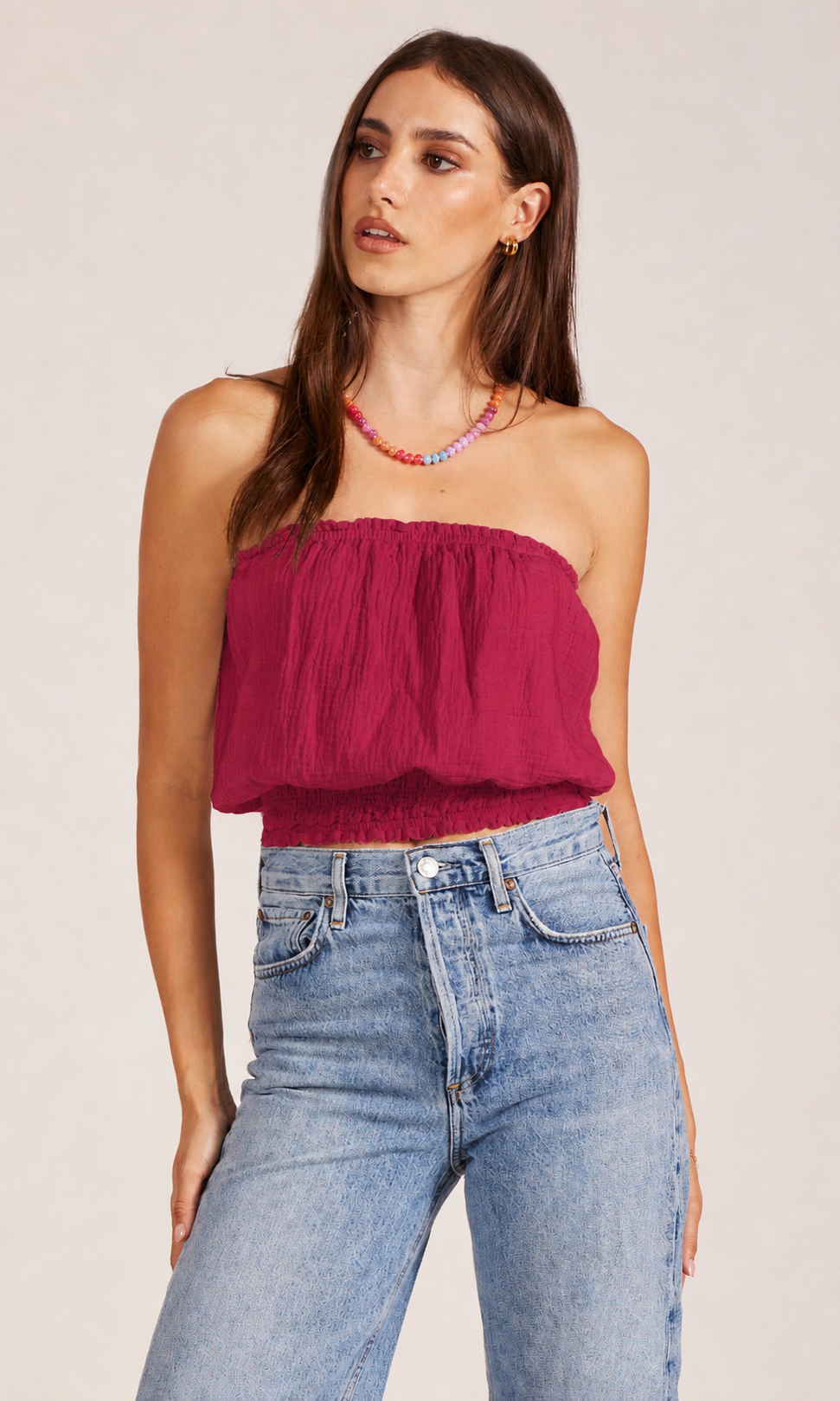 Woman wearing a strapless burgundy top and blue jeans on a plain background