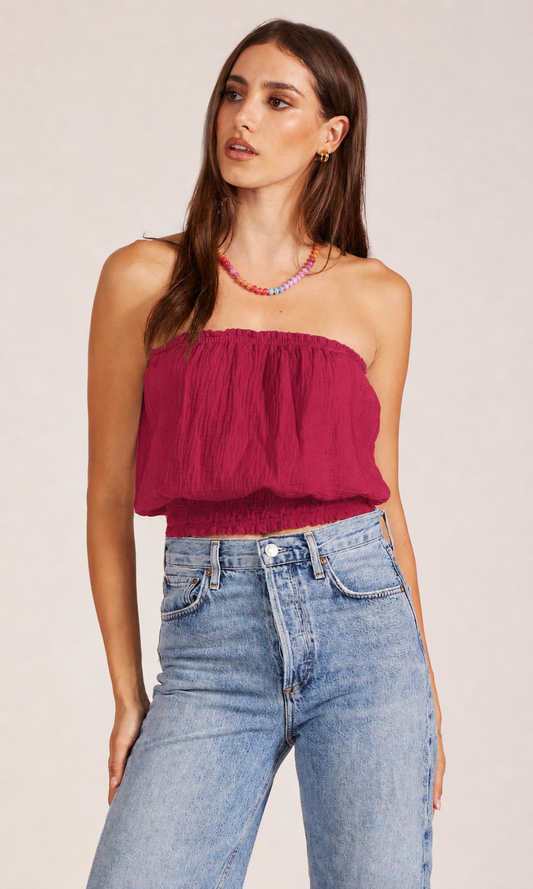 Woman wearing a strapless burgundy top and blue jeans on a plain background