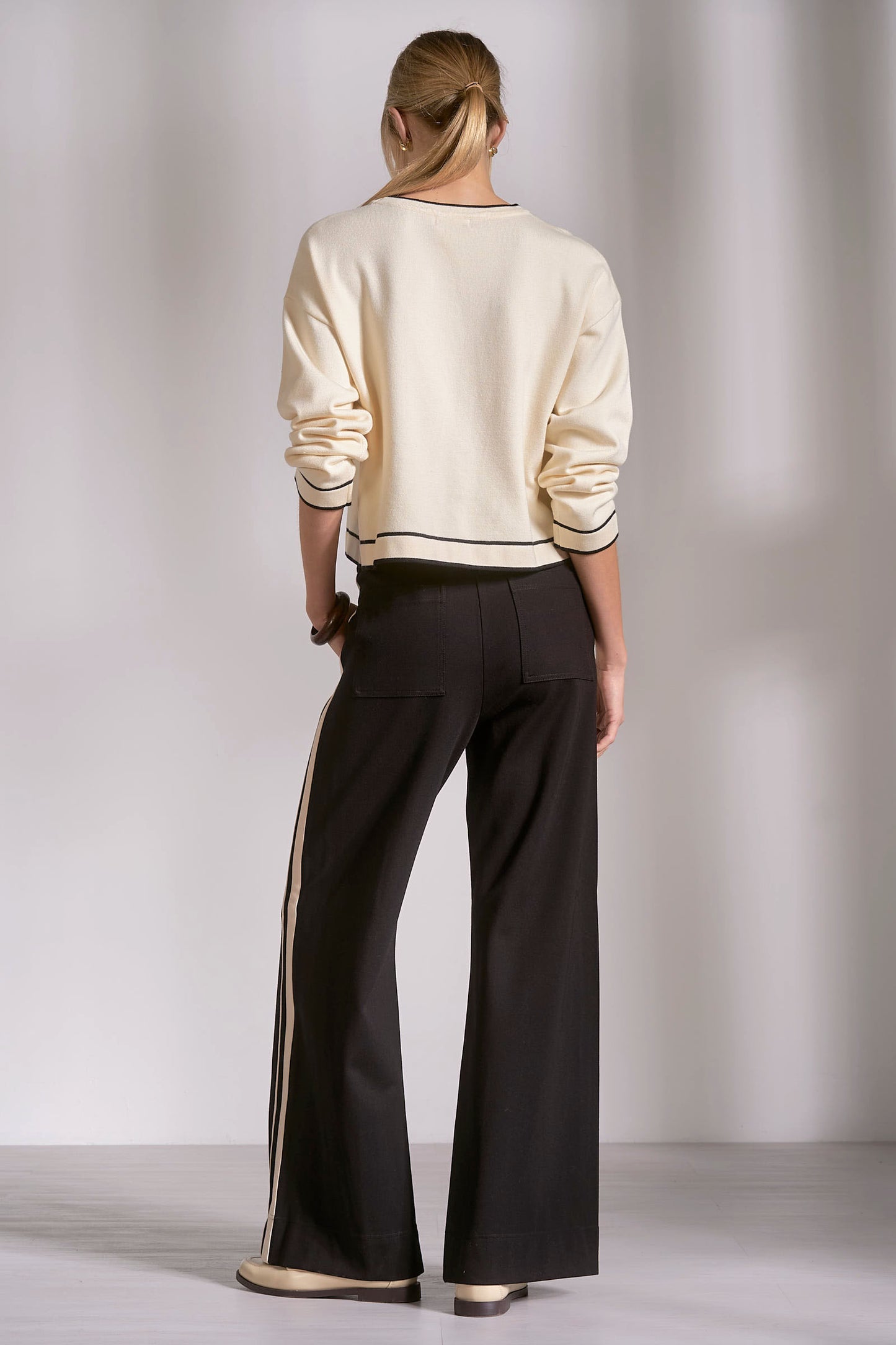 Person wearing a cream sweater and black pants against a plain background