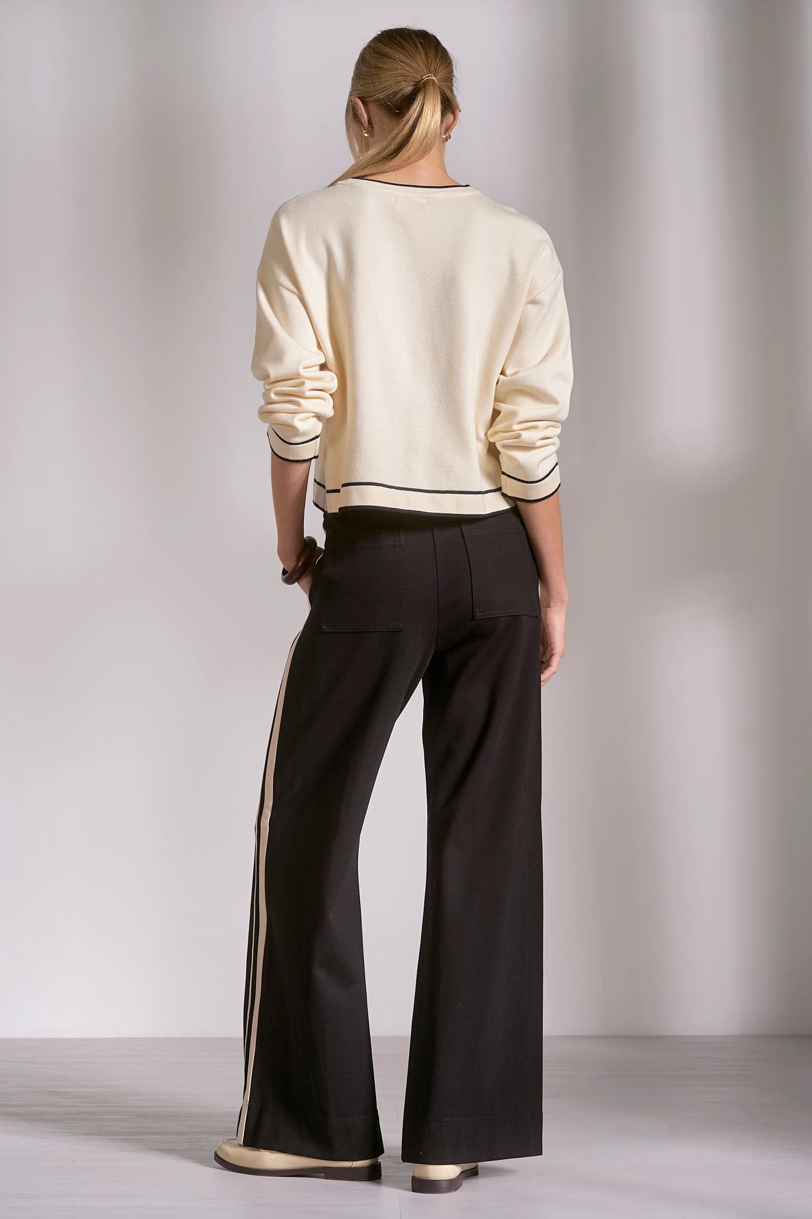 Person wearing a cream sweater and black pants against a plain background