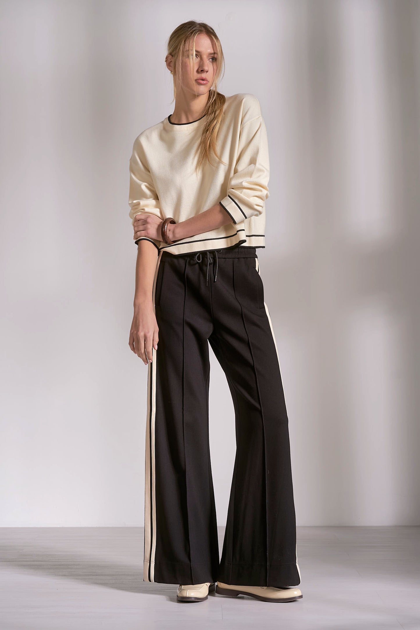 Woman wearing a beige sweater and black pants against a plain background