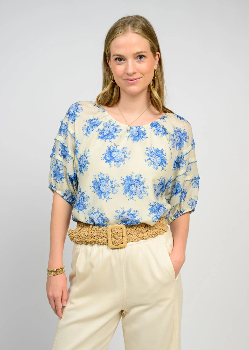 Woman wearing a floral blouse and beige pants against a plain background