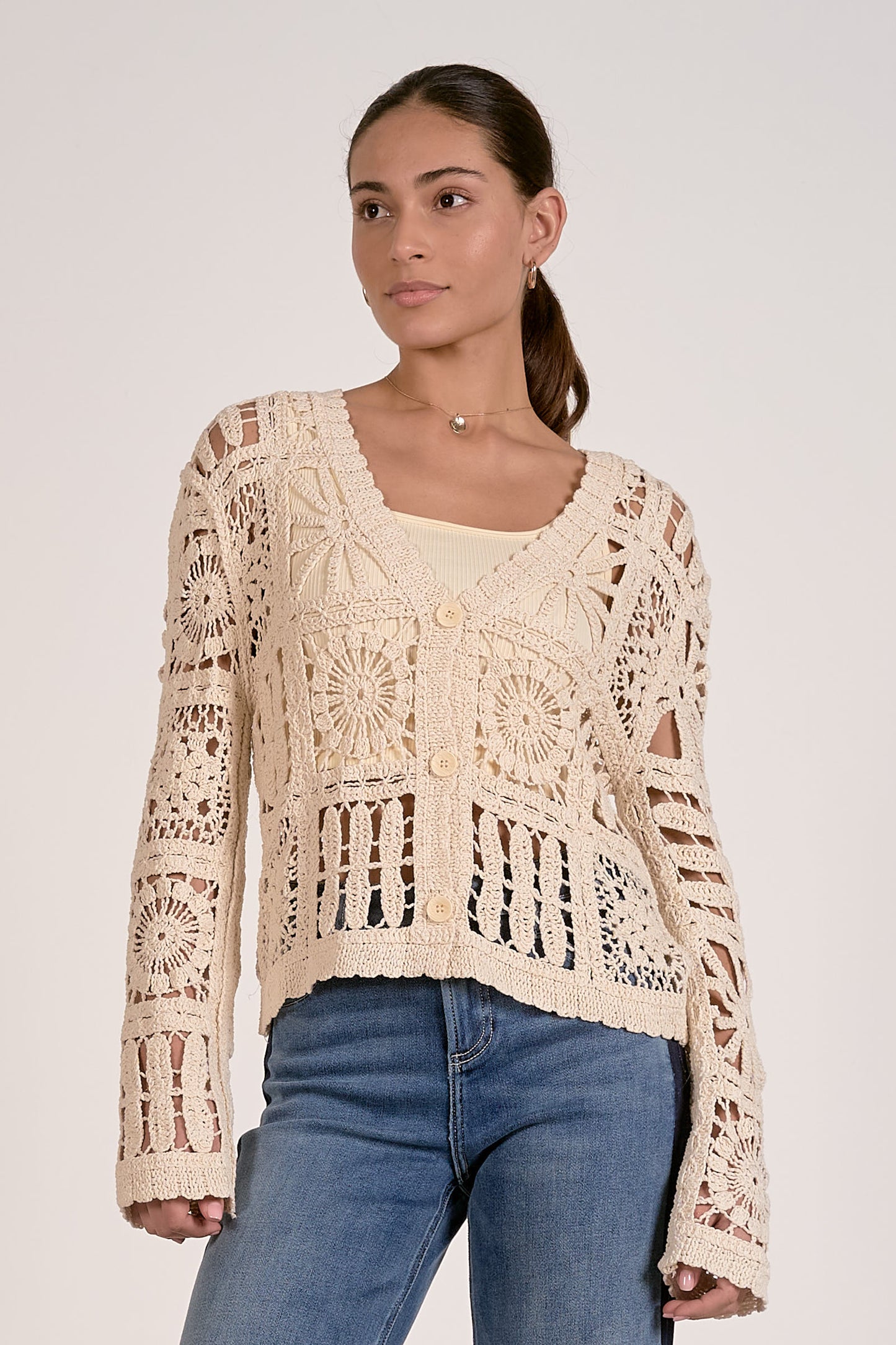 Woman wearing a beige crochet top and blue jeans on a white background