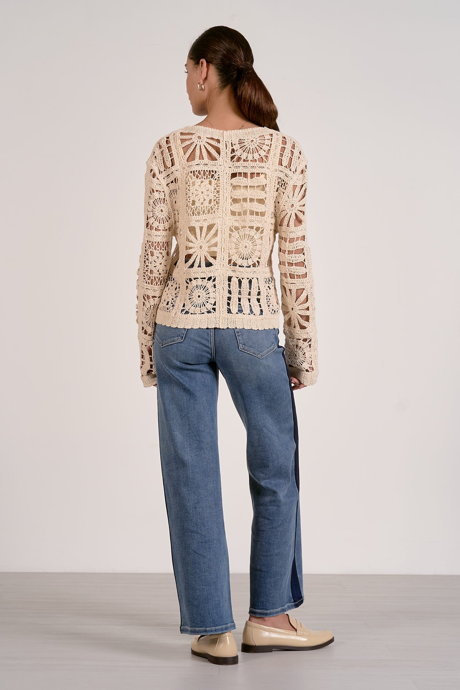 Woman wearing a beige crochet sweater and blue jeans on a plain background