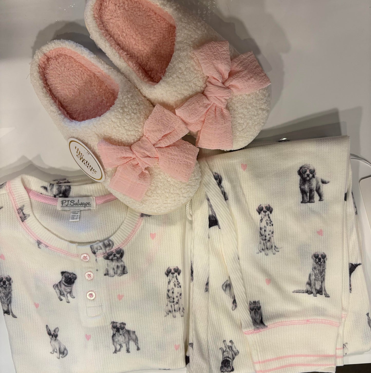 pajama joggers with dog pattern, pink slippers, and blanket on a white background