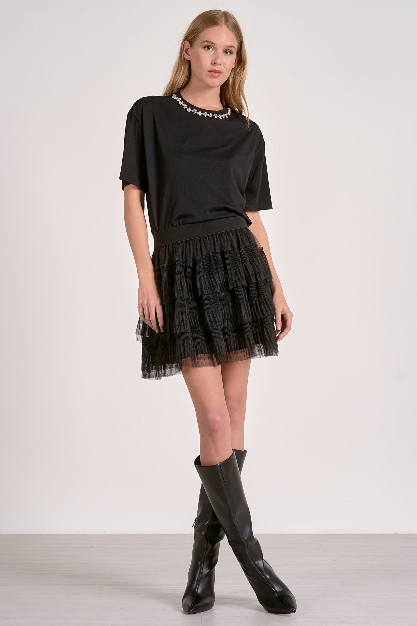 Woman wearing a black outfit with a skirt and boots on a white background