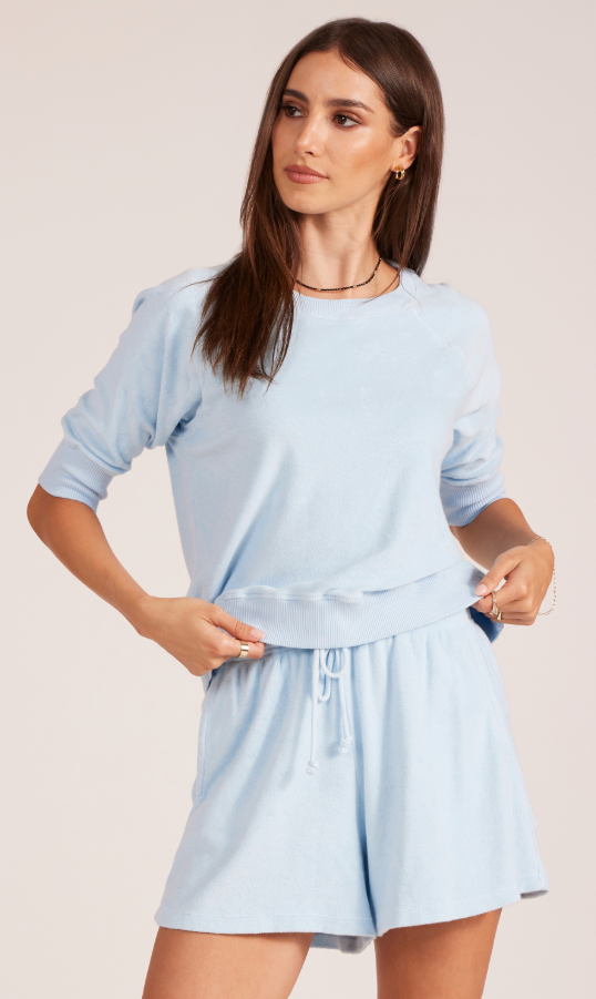 Woman wearing a light blue outfit with a matching top and shorts on a plain background