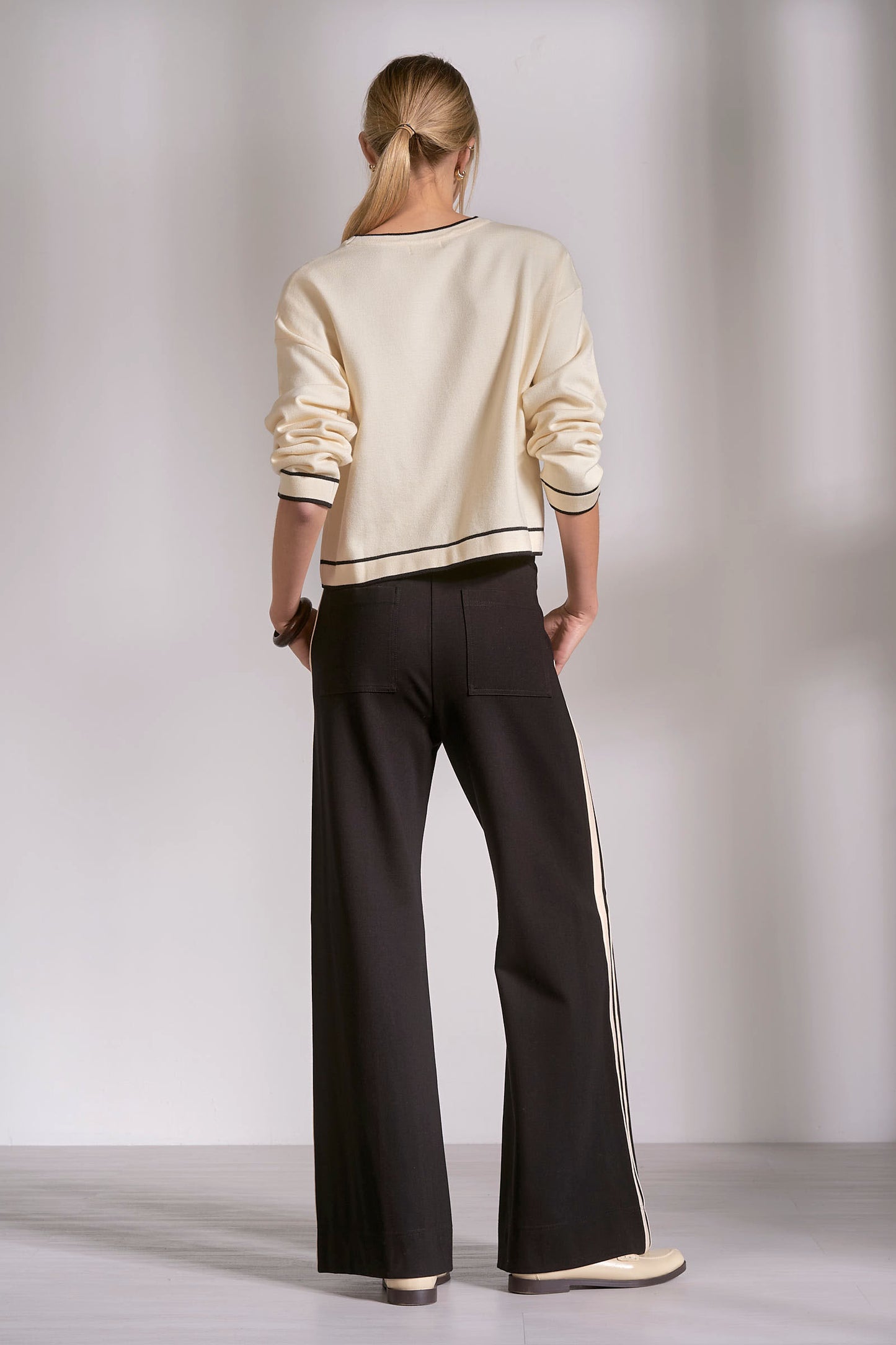Person wearing a cream sweater and black pants against a plain background
