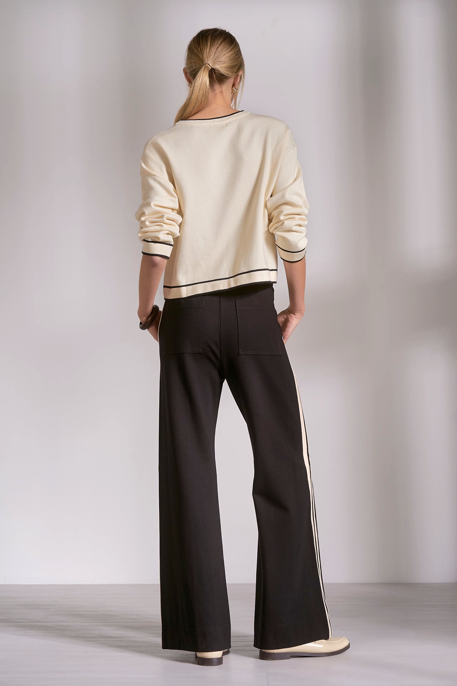 Person wearing a cream sweater and black pants against a plain background
