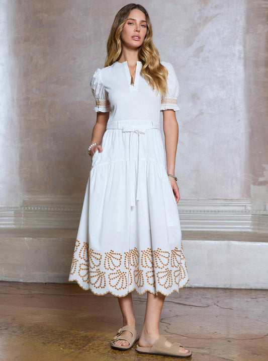 Woman wearing a white dress with lace details against a neutral wall.