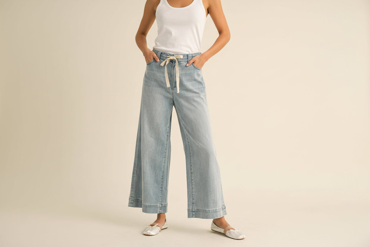 Person wearing light blue denim pants with a white shirt on a beige background