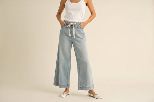Person wearing light blue denim pants with a white shirt on a beige background
