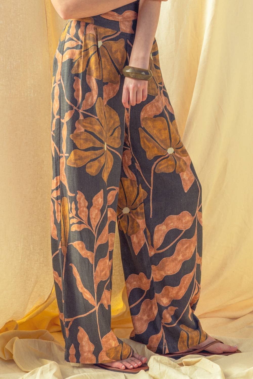 Person wearing a pair of wide-leg pants with a leaf pattern against a beige curtain background