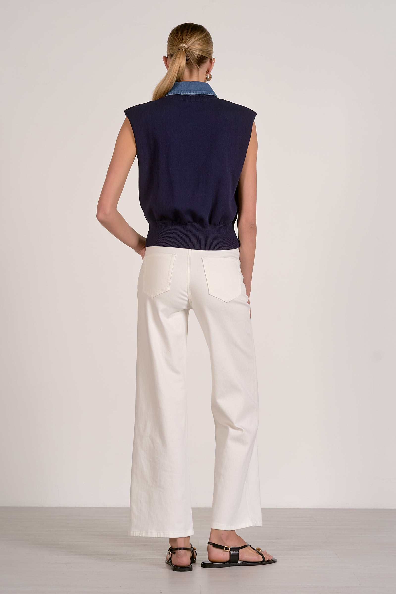 Person wearing a navy sleeveless top and white pants on a plain background