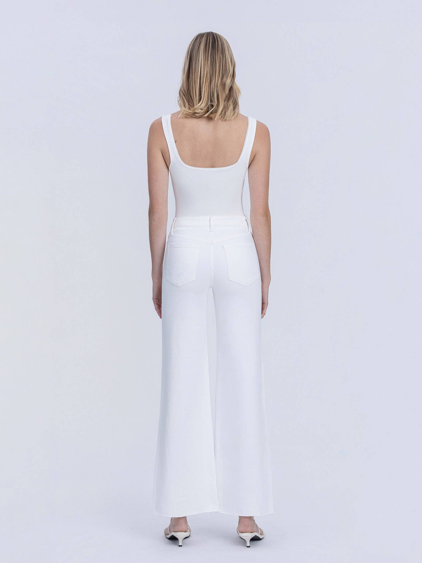 Woman wearing a white sleeveless dress against a plain background