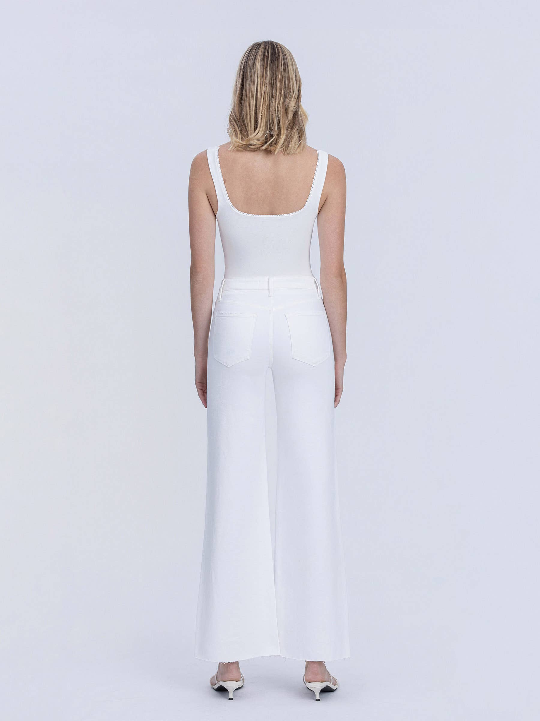 Woman wearing a white sleeveless dress against a plain background