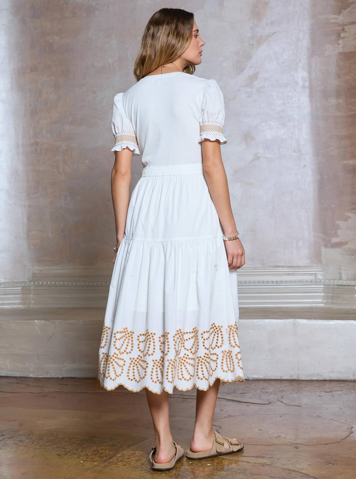 Woman wearing a white dress with lace details in a room with a textured wall.