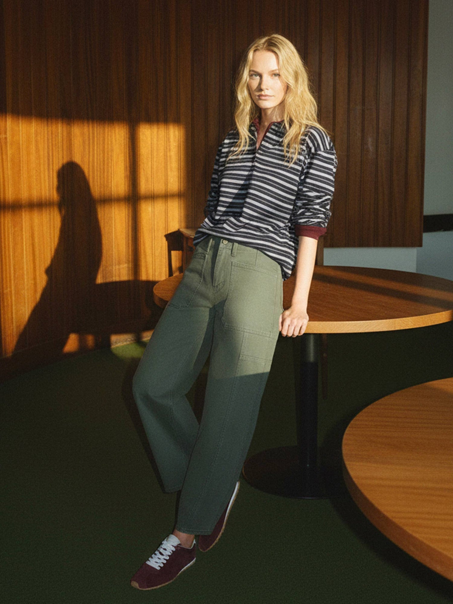 Woman standing in a room with wooden paneling and a table, casting a shadow on the wall.
