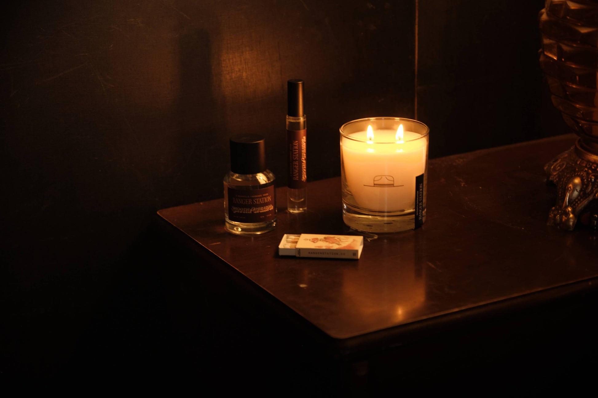 Candle and small bottles on a dark surface with a warm glow.