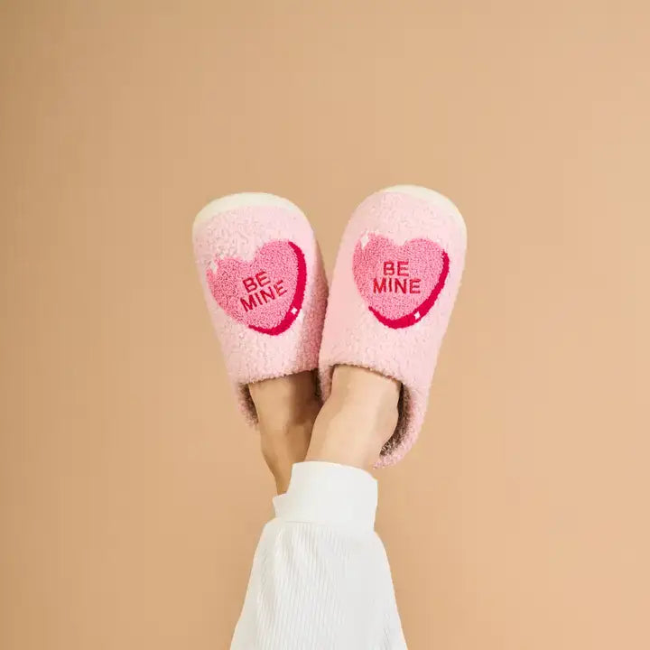 Pink slippers with 'Be Mine' text on a beige background
