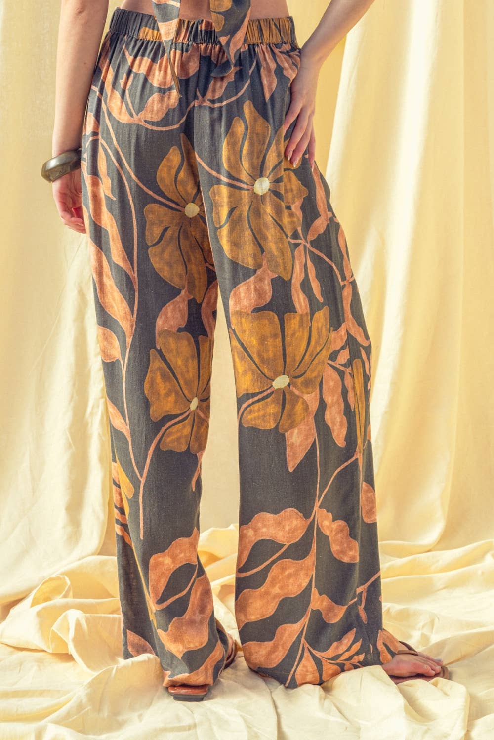 Person wearing floral-patterned pants on a beige fabric background