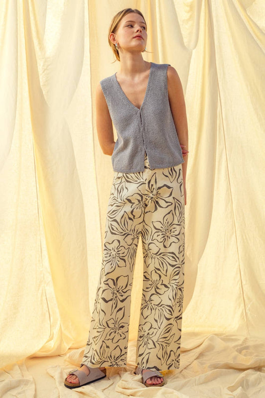 Woman wearing a sleeveless patterned top and floral pants against a light curtain background