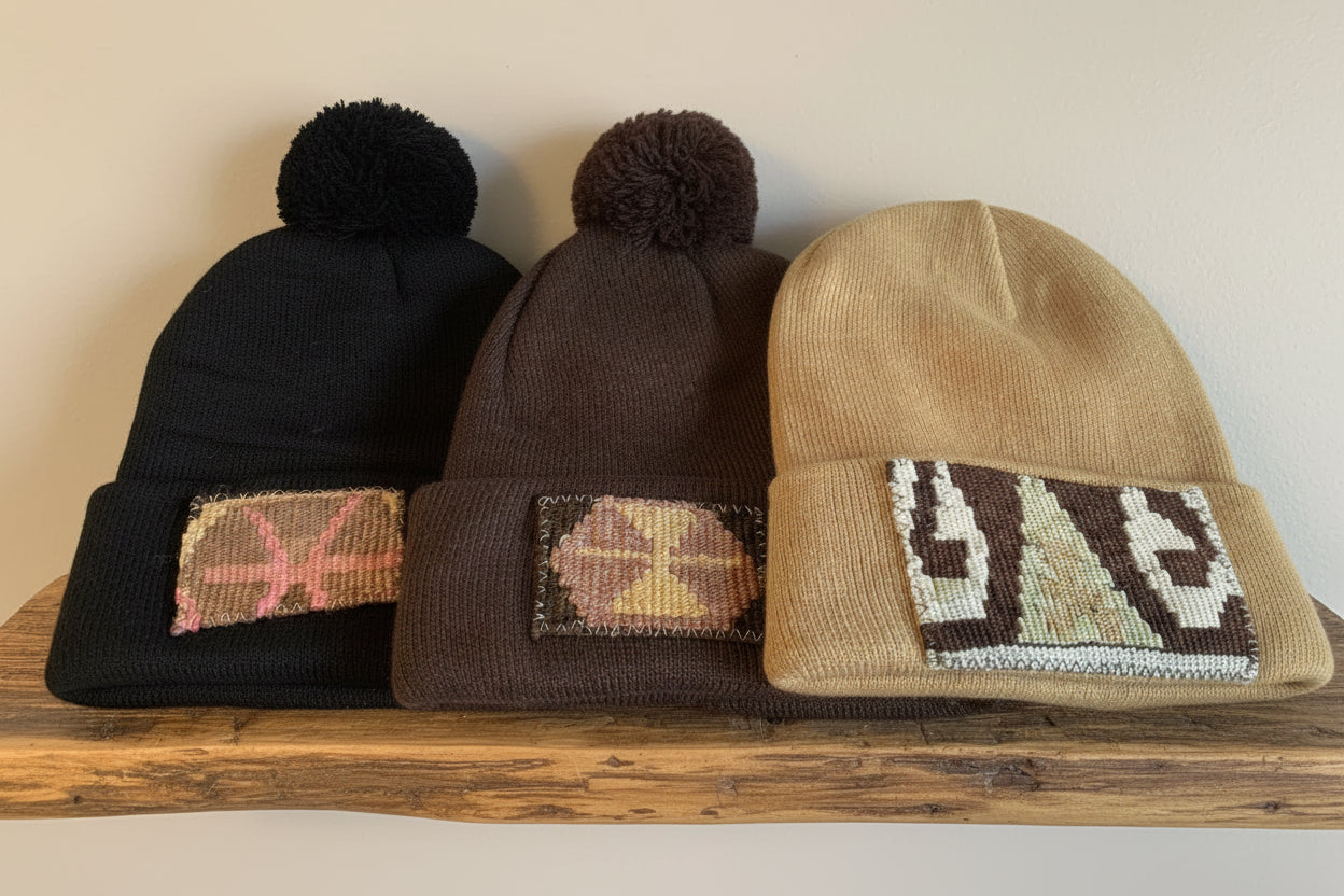 Three beanies in black, brown, and beige with patterned patches on a wooden surface.