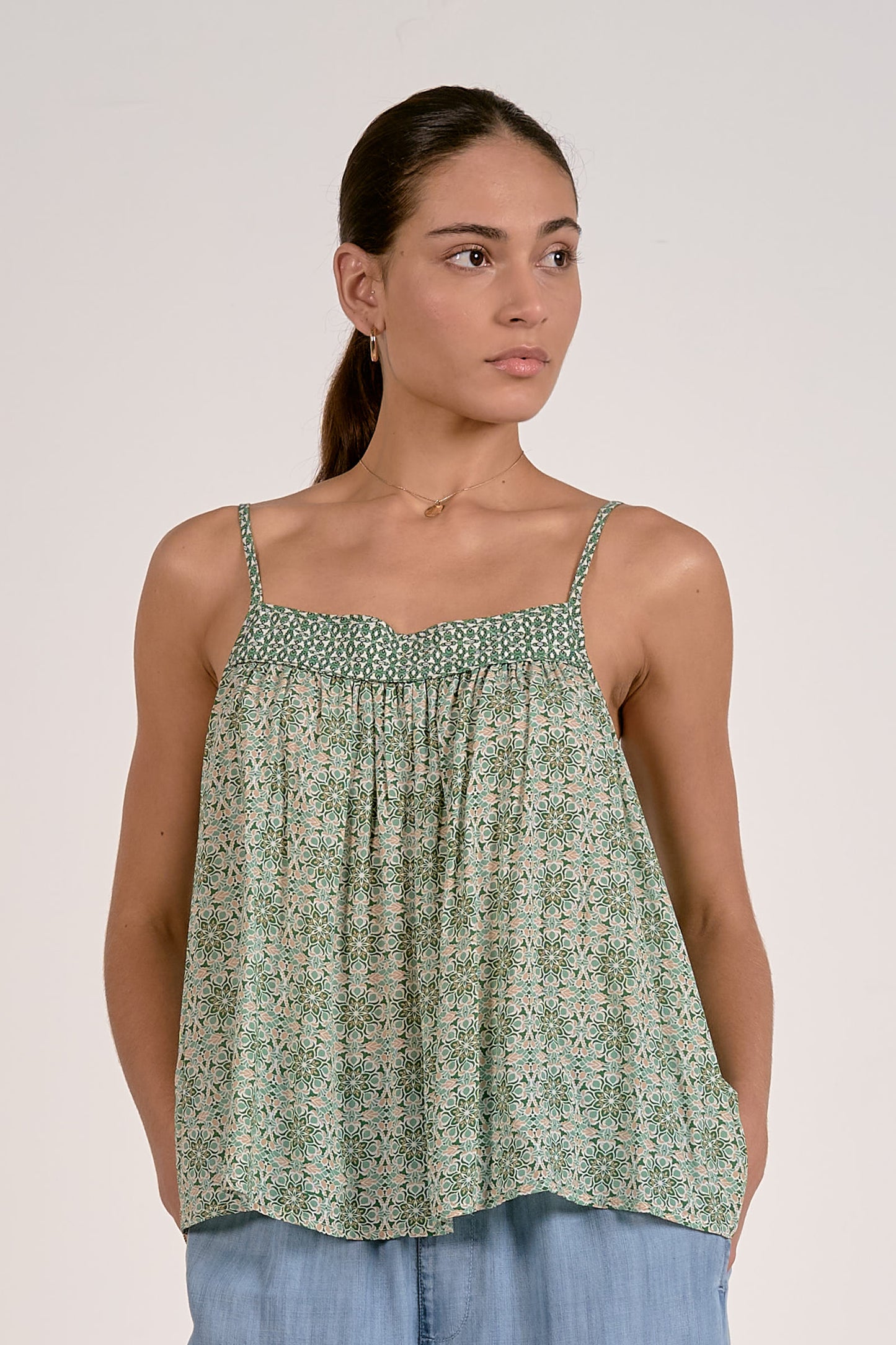 Woman wearing a green patterned top with blue pants against a plain background