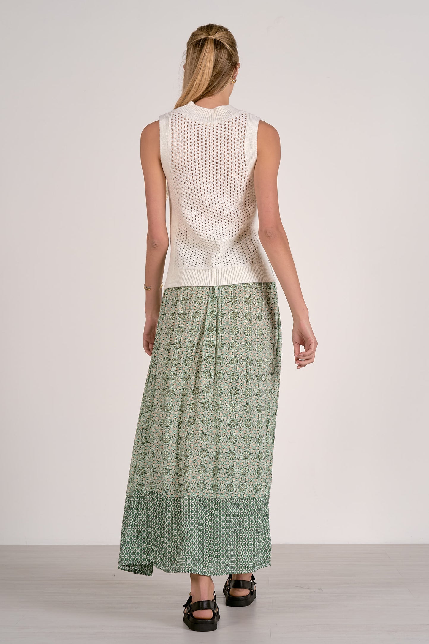 Woman wearing a white sleeveless top and green patterned skirt on a plain background