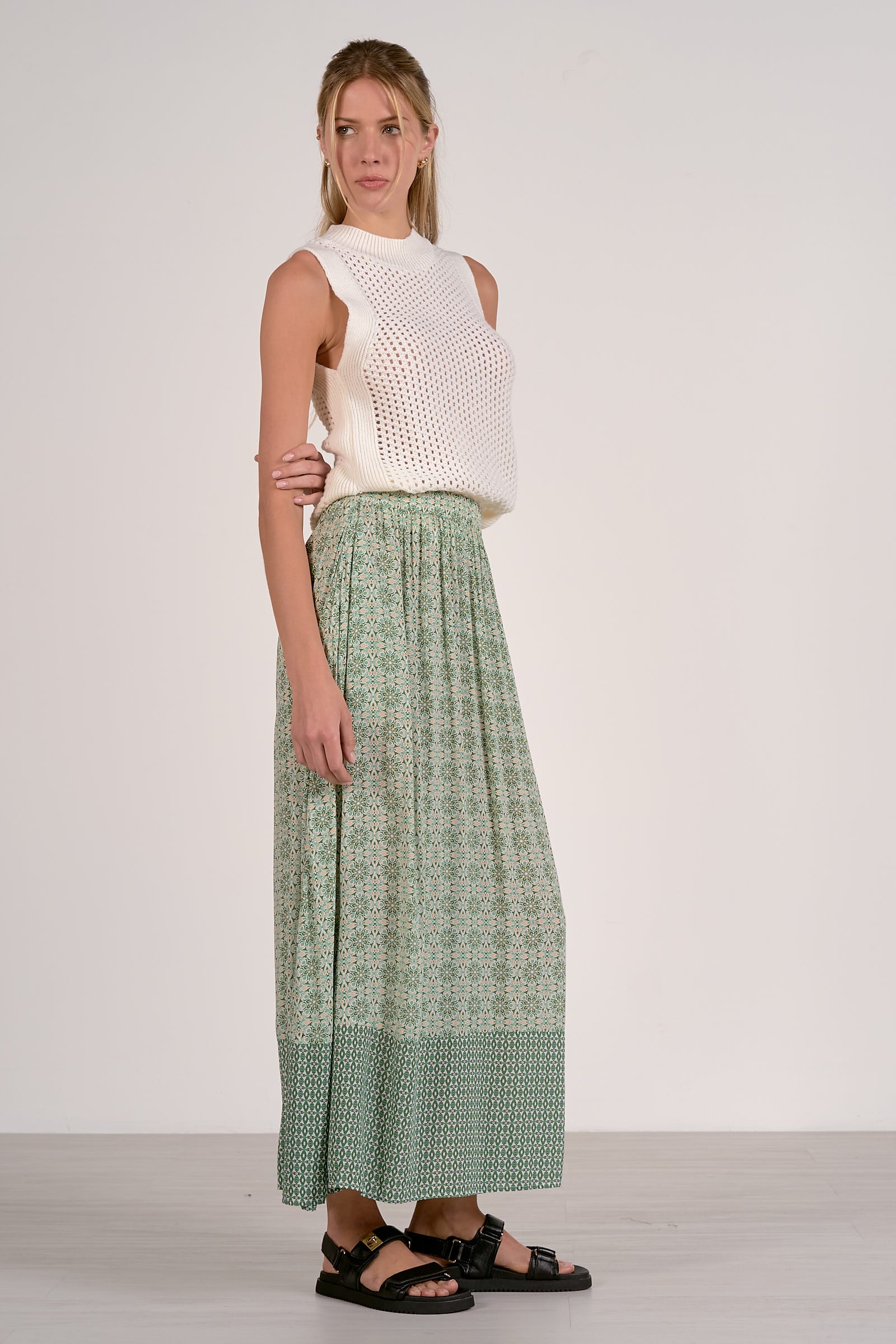 Woman wearing a white sleeveless top and green patterned pants on a white background