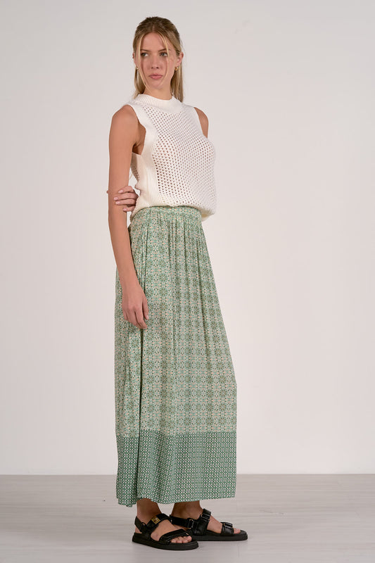 Woman wearing a white sleeveless top and green patterned pants on a white background