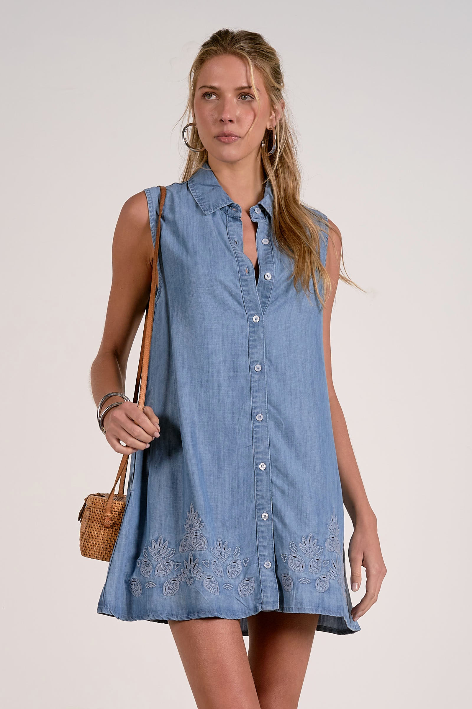 Woman wearing a blue denim dress with floral embroidery on a plain background