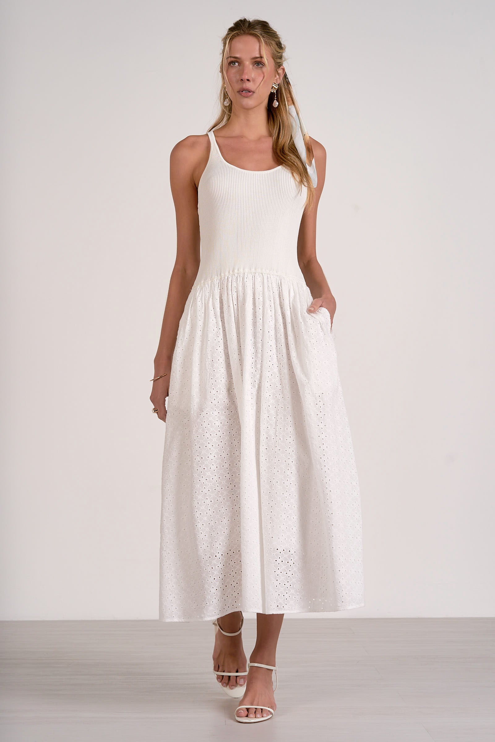 Woman wearing a white sleeveless dress with lace details on a plain background
